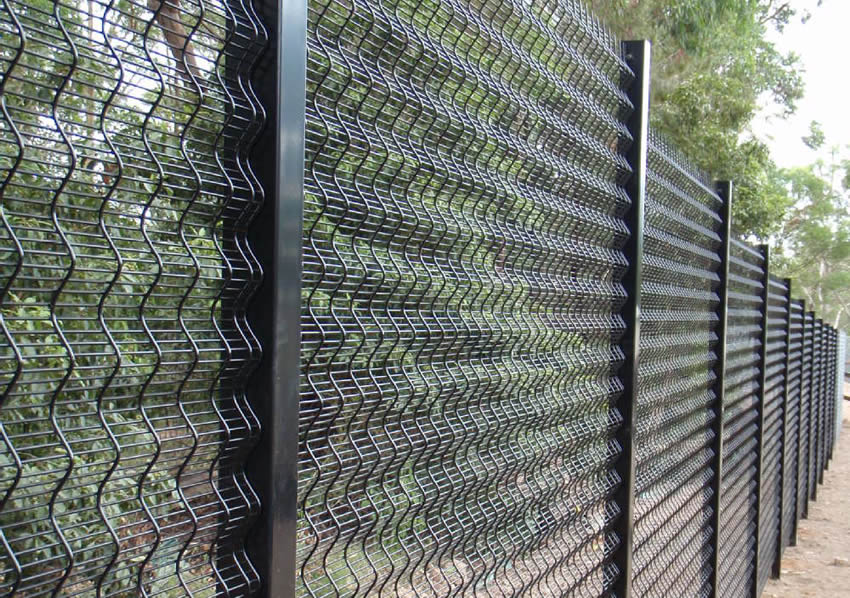 Black polyester coated curved security fencing separates old trees from the road.
