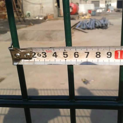 A worker is measuring the hole width of twin wire fence by meter ruler.